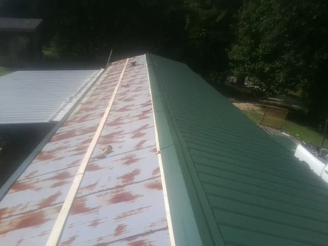 Old rusted panels beside newly installed green metal roofing — Wind Damage Roof Repair by Roofing Brothers in Kellogg
