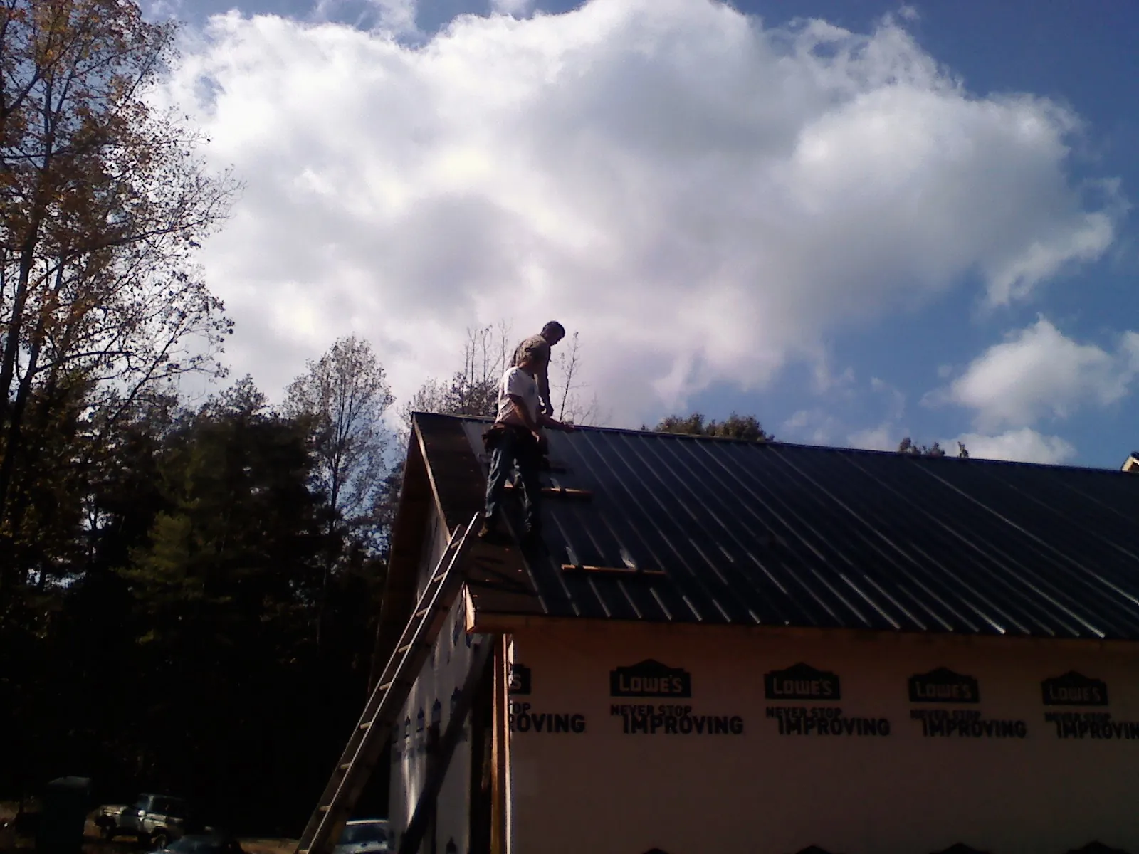 Roofer fastening dark metal panels high against a cloudy sky, from a Roof Inspection job in Kellogg